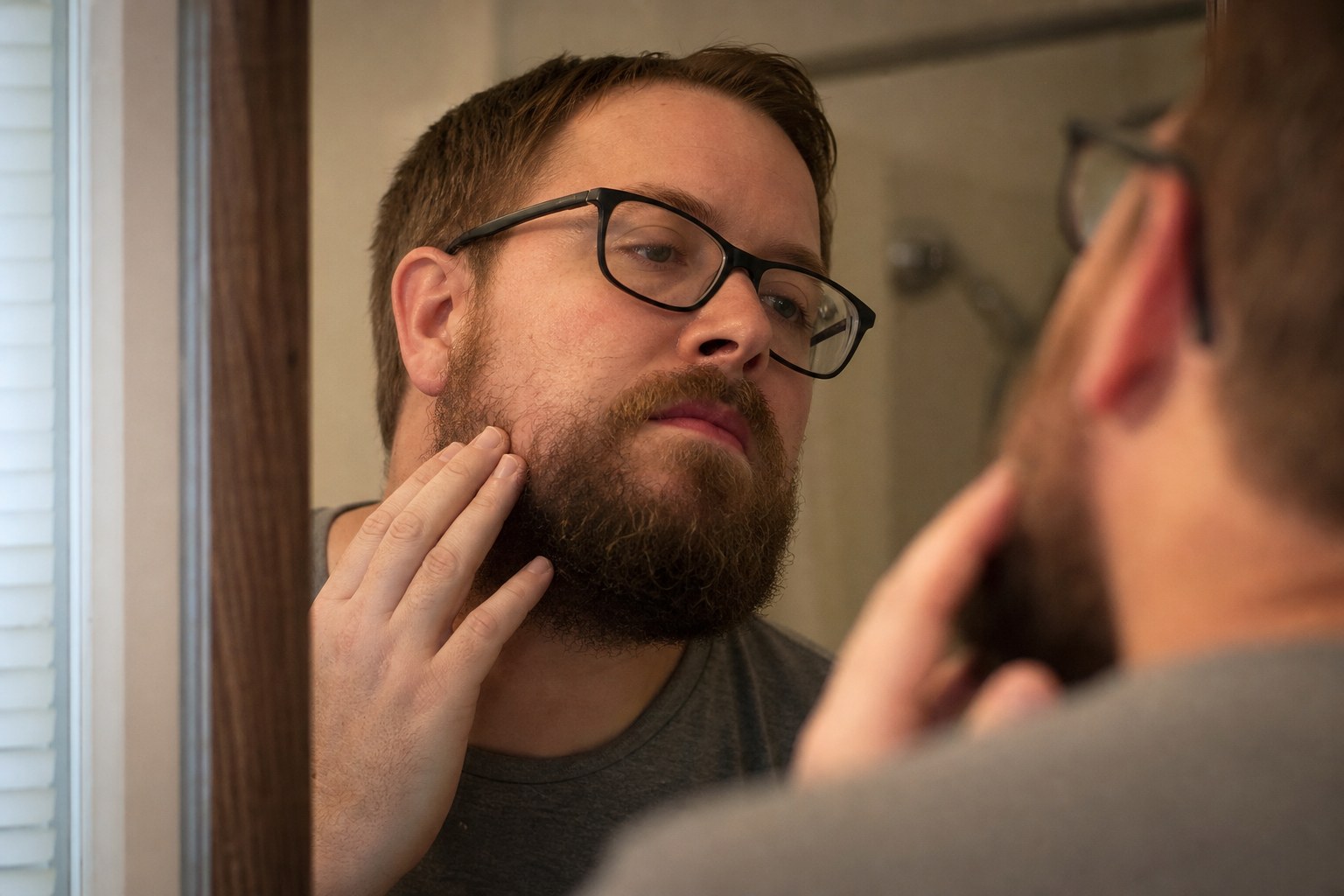 Bearded man checking a sparse patch along his cheek line in the mirror